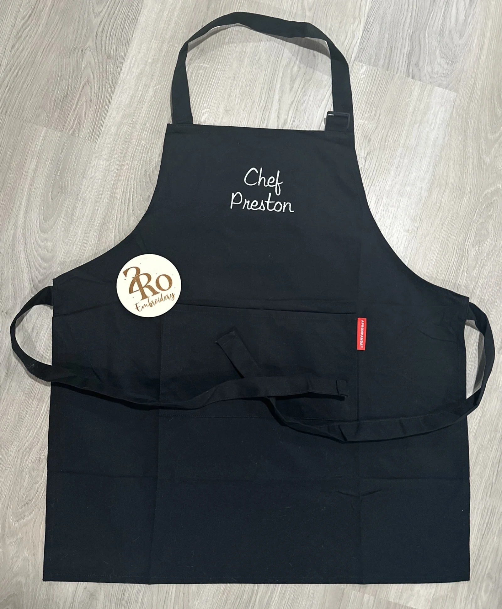 Black apron embroidered with Chef and a first name in white script