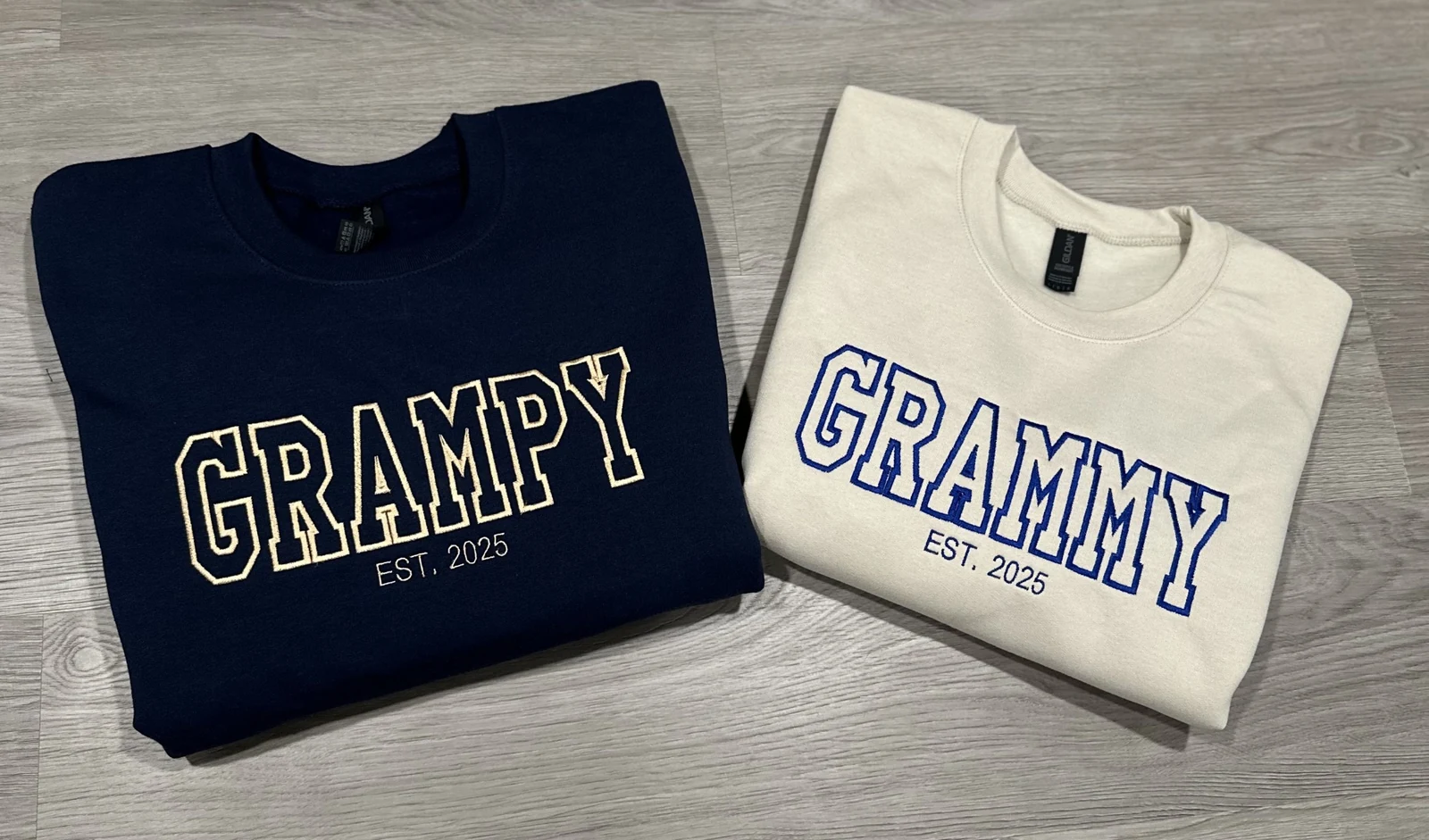 Navy GRAMPY and cream GRAMMY sweatshirts with outlined varsity lettering and EST. 2025