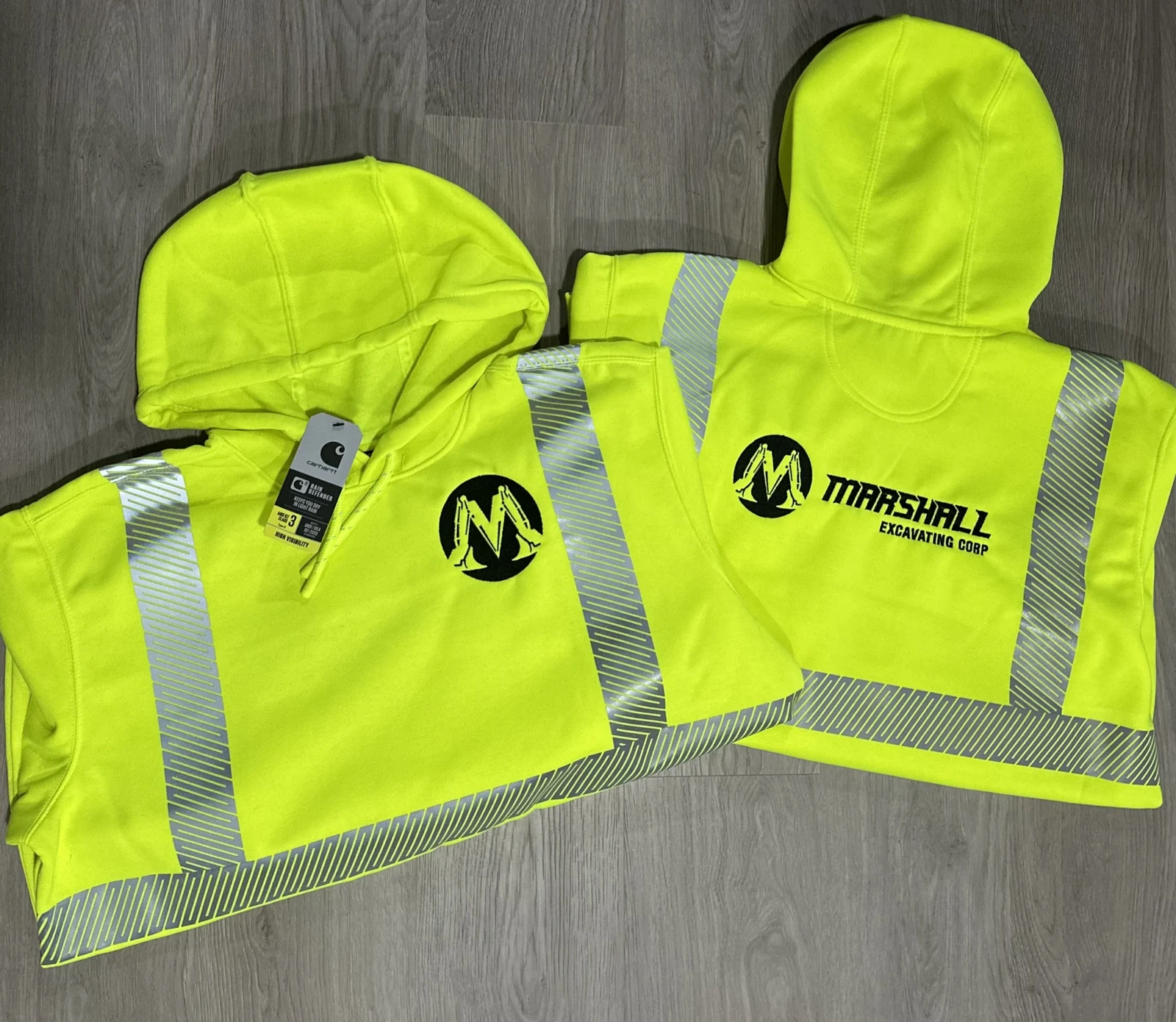 Two safety-yellow reflective hoodies with the black Marshall Excavating Corp logo embroidered on the front and back