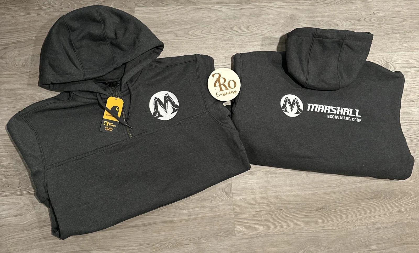 Two charcoal hoodies with the white Marshall Excavating Corp logo embroidered on the front and back