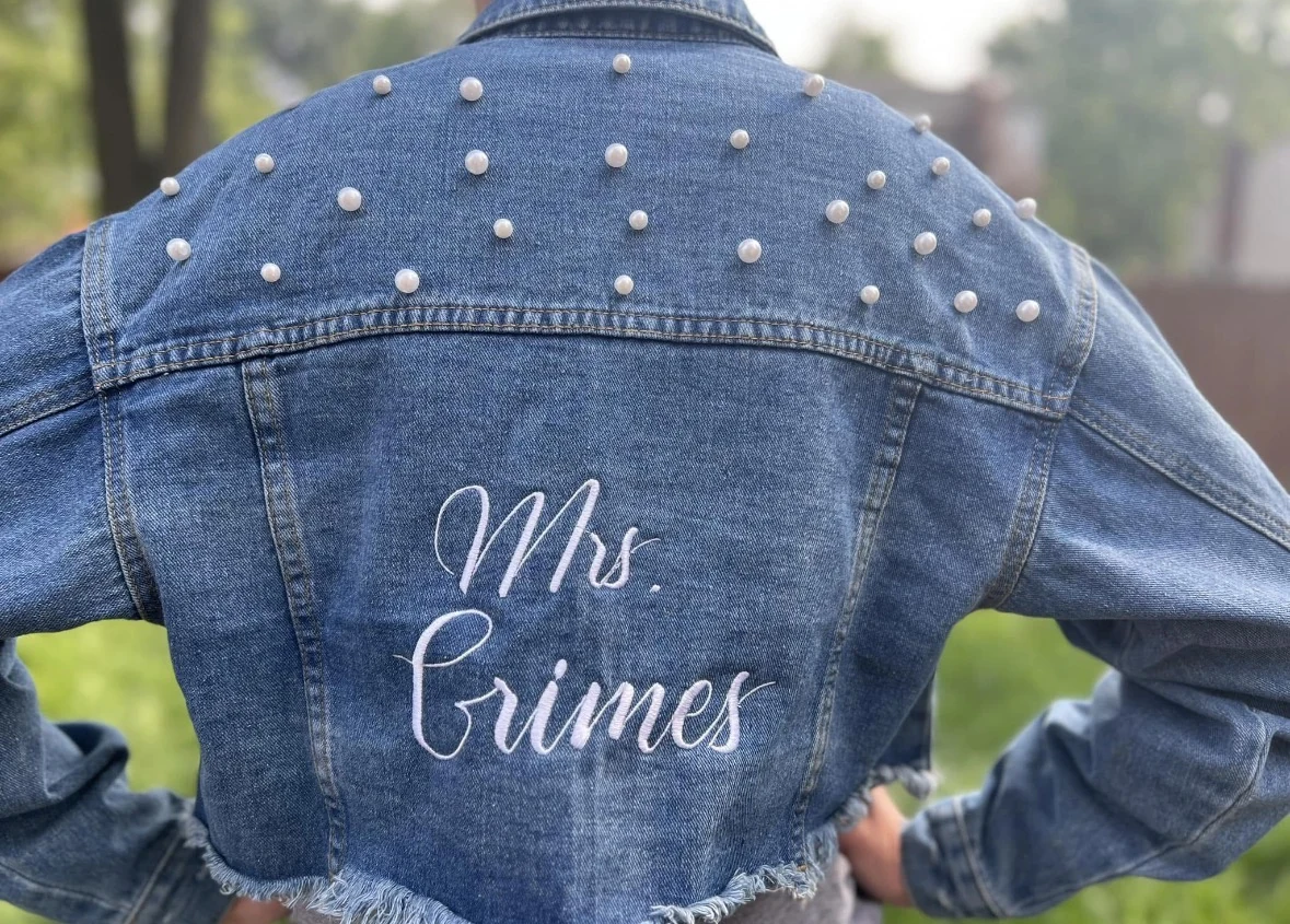 Back of a cropped, pearl-studded denim jacket embroidered with Mrs. and a last name in white script