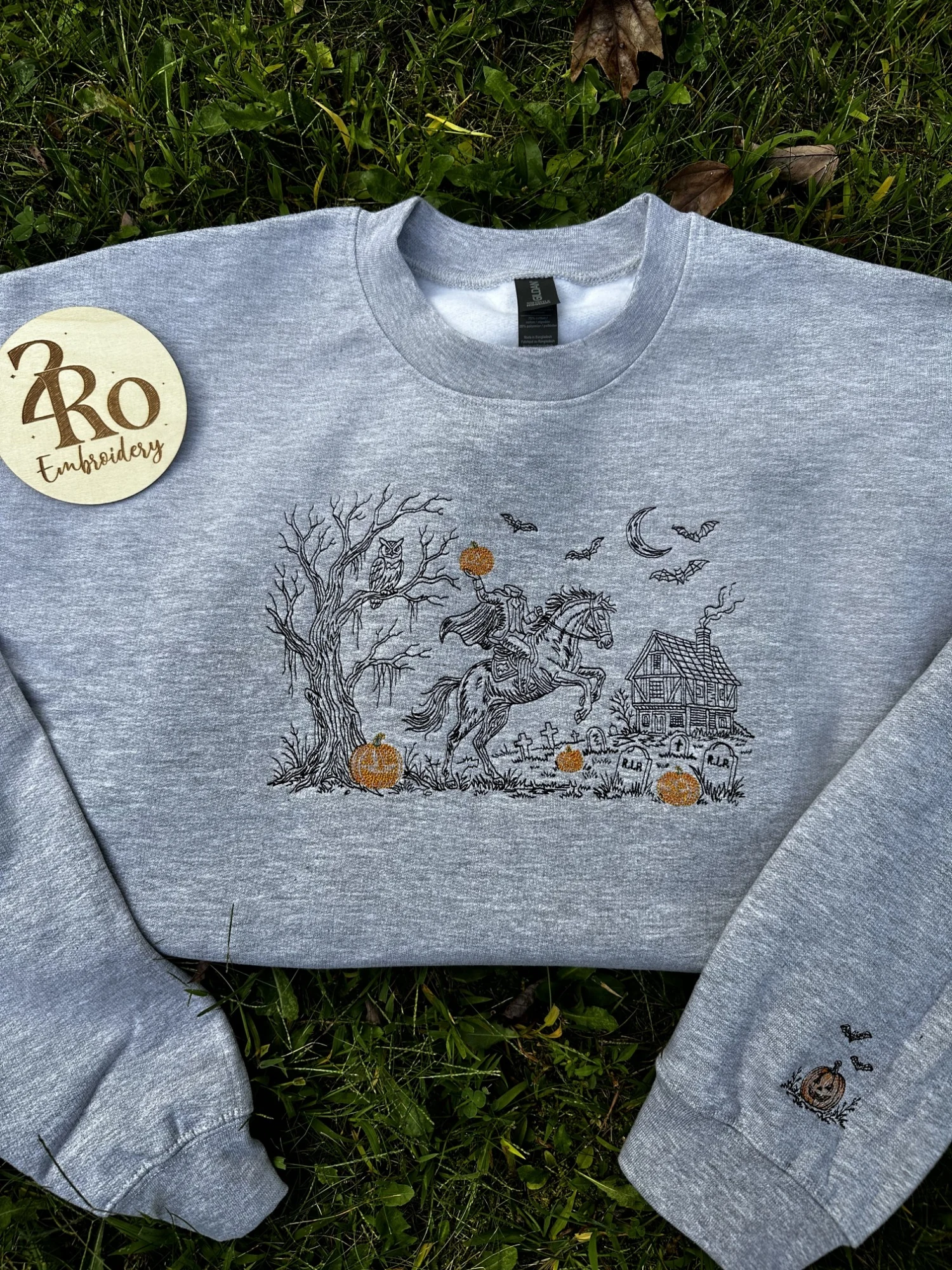 Gray sweatshirt embroidered with a black-thread headless horseman scene, orange pumpkins, and a small pumpkin on the sleeve cuff