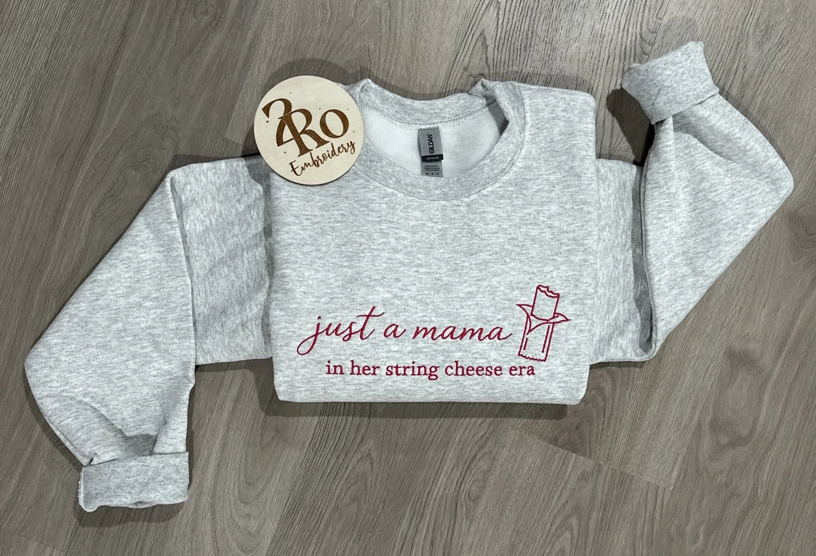 Ash sweatshirt embroidered in raspberry with just a mama in her string cheese era and a string cheese sketch