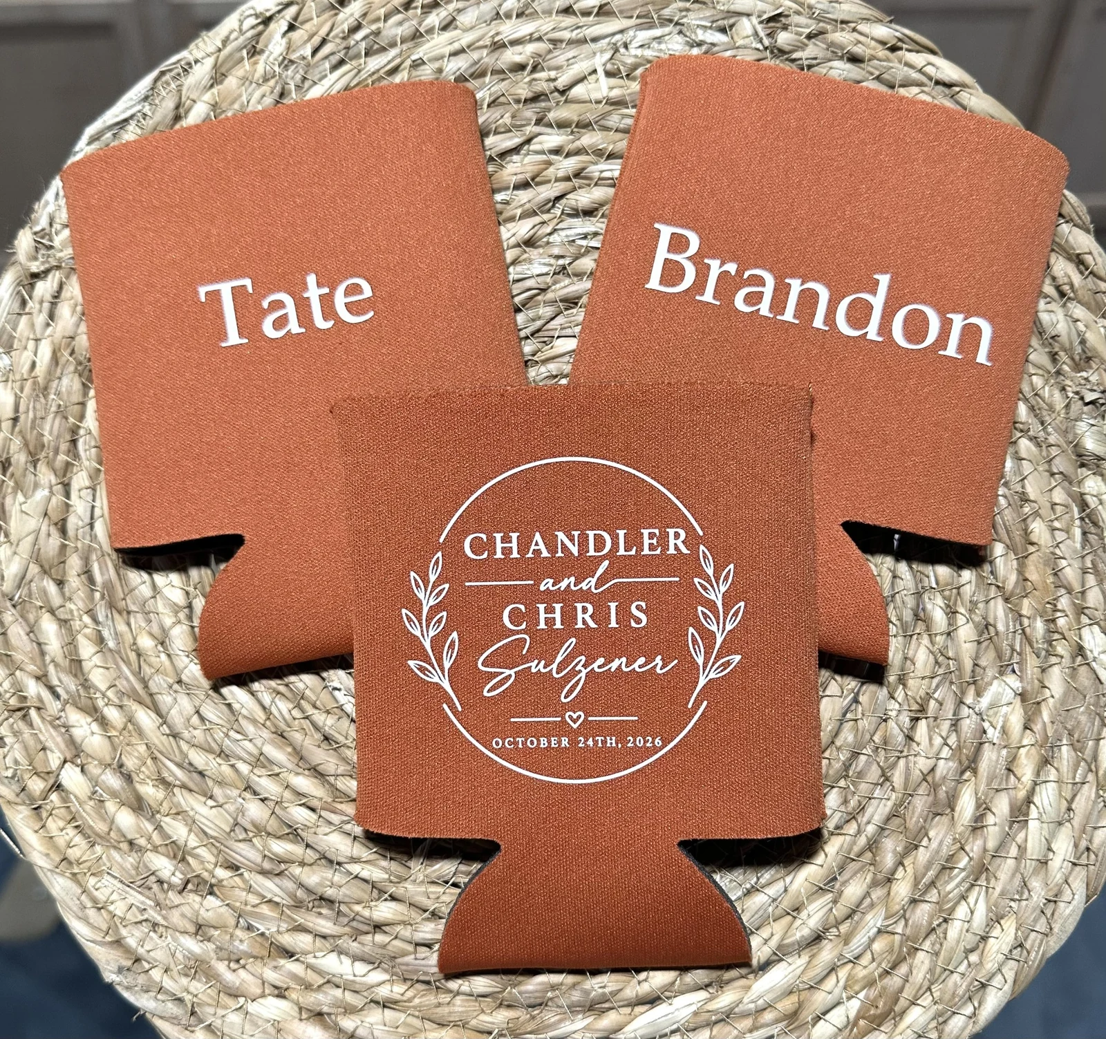 Three rust-colored can koozies printed in white with two names and a wedding monogram